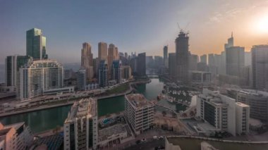 Gün doğumundan itibaren Dubai Marina 'da limana park edilmiş tekne ve yatlar ve kanalın etrafında gökdelenler var. Gölgeler hızlı hareket ediyor. Arka planda JBR bölgesi kuleleri