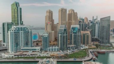 Dubai Marina 'da limanda yeşil çimlerin yanında birkaç tekne ve kanal havası etrafında gökdelenler. Gün be gece geçiş zamanı. Arka planda JBR bölgesi kuleleri