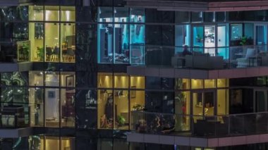 Çok katlı binaların büyük pencerelerinde, çok renkli ışıklardan oluşan düz bir panorama. Büyük bir şehirde aydınlık bir gökdelen.