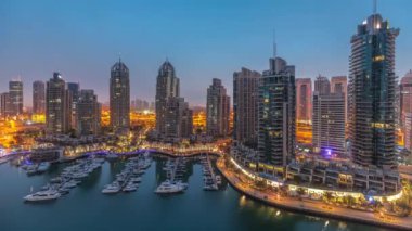 Gündoğumundan önce Dubai marinasında gece gündüz lüks yat hangarında geçiş zamanı. Rıhtım boyunca modern gökdelenler ve limanda yüzen tekneler.