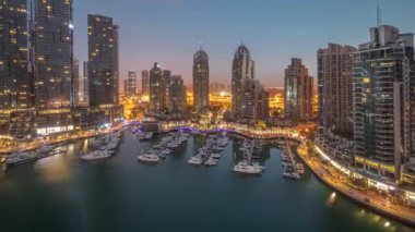 Gündoğumundan önce Dubai marinası panoramasında gece gündüz lüks yat hangarında geçiş zamanı. Rıhtım boyunca modern gökdelenler ve limanda yüzen tekneler.