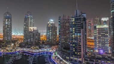 Panorama, Dubai marinasında gece hava sahasında lüks yat hangarını gösteriyor. Rıhtım boyunca modern gökdelenler ve limanda yüzen tekneler.