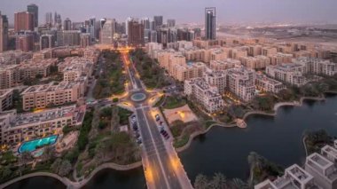 Barsha Heights bölgesindeki gökdelenler ve Greenens bölgesindeki alçak binalar hava gününden geceye geçiş zamanları. Palmiyeleri ve yürüyen göleti olan Dubai silüeti