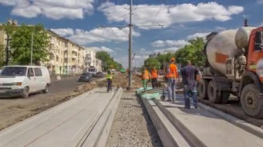 Yol onarımı için plakaların arasına beton dökülüyor. Bir sürü işçi ve mikser makinası var. Tramvay raylarının yeniden inşası