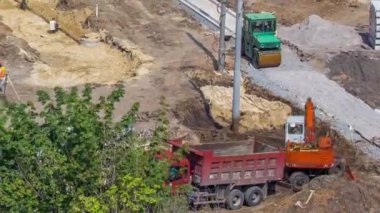 Endüstriyel kamyon kazıcısı ve buldozer toprağı hareket ettiriyor ve yol inşaatındaki bir çöp kamyonuna yüklüyor. Beton plakalı tramvay raylarının hava görüntüsü