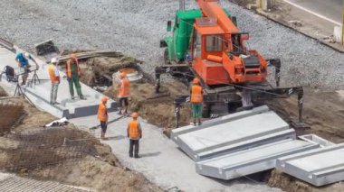 Yol inşaatı zamanına vinçle beton plakalar yerleştiriliyor. Şapkalı ve üniformalı endüstriyel işçiler. Havadan görünüşlü. Şehir Bulvarı 'ndaki tramvay raylarının yeniden inşası