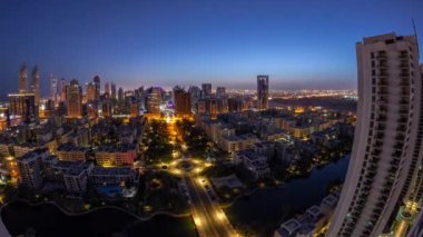 Barsha Heights bölgesindeki gökdelenler ve Greenens bölgesindeki alçak binalar gece gündüz geçiş zamanı panorama. Palmiyeler ve ağaçlarla Dubai silueti