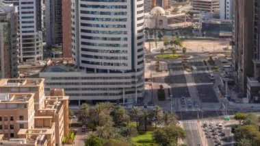 Barsha Heights bölgesindeki gökdelenler ve camii ve Yeşiller bölgesindeki alçak katlı binalar gölgeler hızla hareket ediyor. Kavşağın etrafında palmiyeler ve ağaçlarla Dubai silüeti