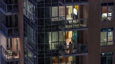 Apartman binasındaki parlayan panoramik pencerelerin gece görüşü. Odalarında ışıklar olan yüksek gökdelenli.