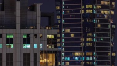 Gece karanlığa bürünmüş gökdelenin panoramik pencereleri şehrin ışıklarının yansımasıyla parlıyor. Aydınlatılmış kuleler