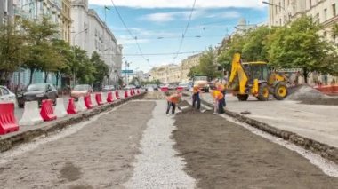 Buldozer hareket eder ve zamanı gelince toprağı ve molozu yayar. Tramvay raylarının yeniden inşasında turuncu üniformalı işçiler. Sokakta trafik vardı. Yol yapım aşamasında.