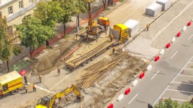 Turuncu inşaat teleskopik vinç eski tramvay raylarını kamyon saatine yüklüyor. Şapkalı ve üniformalı endüstriyel işçiler. Şehir caddesindeki tramvay raylarının yeniden inşası