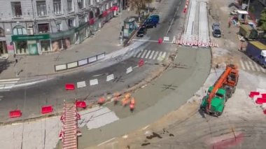 Beton, turuncu üniformalı ve vinçli işçilerin bulunduğu yol inşaatında çalışıyor. Yukarıdan tramvay raylarının yeniden inşası