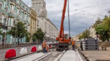 Yol inşaatı zamanına vinçle beton plakalar yerleştiriliyor. Şapkalı ve üniformalı endüstriyel işçiler. Şehir caddesindeki tramvay raylarının yeniden inşası. Bulutlu gökyüzü