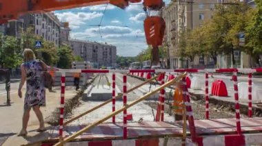 Portakal rengi teleskopik hareketli vinç takviye zaman aralığında küçük yaya köprüsünü hareket ettiriyor. Şapkalı ve üniformalı endüstriyel işçiler. Şehir caddesindeki tramvay raylarının yeniden inşası