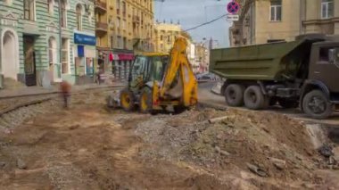Endüstriyel sarı kazıcı toprağı taşıyor ve yol inşaatındaki bir çöp kamyonuna yüklüyor. Kavşaktaki tramvay raylarının yeniden yapılandırılmasının görüntüsü