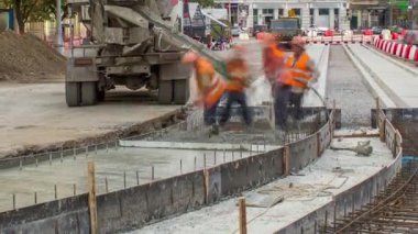 Beton, turuncu üniformalı ve mikser makineli birçok işçiyle yol inşaatı için özel plakaların yanında çalışıyor. Tramvay raylarının yeniden inşası