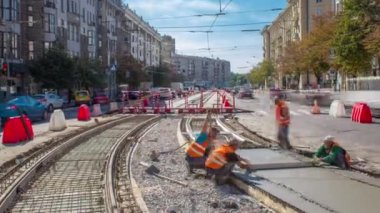 Bir yol inşaatında beton döşeme, turuncu üniformalı birçok işçi ve şehir trafiği. Tramvay raylarının yeniden inşası