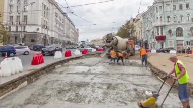Turuncu üniformalı ve mikser makineli işçilerle yol inşaatı için somut çalışmalar ve sıkıştırma. Tramvay raylarının yeniden inşası