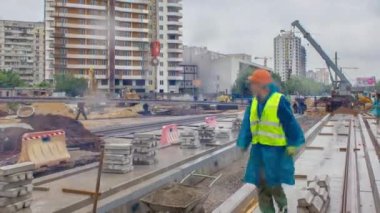 Gri inşaat teleskopik vinç beton plakalara zaman ayarlı tramvay raylarını boşaltıyor. Şapkalı ve üniformalı endüstriyel işçiler. Tramvay raylarının yeniden inşası