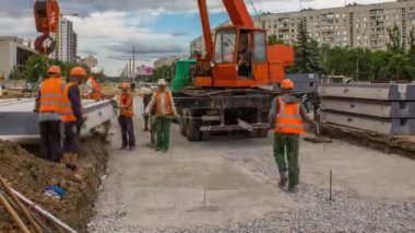 Yol inşaatında vinçle ezilmiş taşın üzerine beton plakalar yerleştiriliyor. Şapkalı ve üniformalı endüstriyel işçiler. Şehir caddesindeki tramvay raylarının yeniden inşası