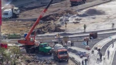 Beton yol yapımında çalışıyor. Üniformalı birçok işçi ve mikser makineli vinç var. Tramvay raylarının yeniden inşası