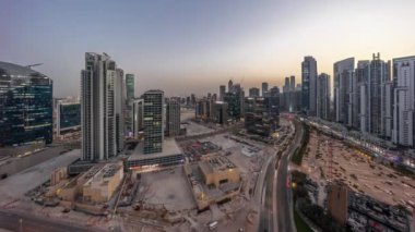Modern kuleleri olan Business Bay 'de konut geliştirme panoramik havadan geceye geçiş zamanı, Dubai, BAE. Gün batımından sonra büyük otoparkın yakınındaki yolda trafiği olan gökdelenler.