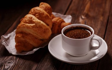 Koyu ahşap masada bir fincan taze kahve ve lezzetli kruvasan. Tatlı ve lezzetli bir kahvaltı..