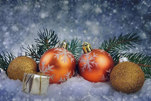 Mutlu yıllar bayramı ya da Noel arkaplanı. Noel baloları, içinde hediyeler olan küçük bir kutu, kardaki şenlikli kurdele ve köknar dalları koyu mavi arka planda..