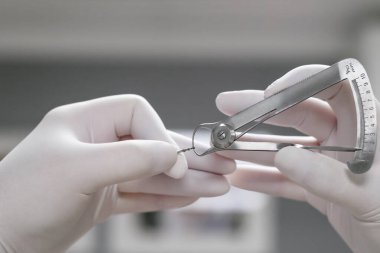 Diş hekiminin elleri beyaz lateks eldivenli, diş ölçer, mikrometre ile ölçülmüş, seçici odaklı. Diş tedavisi için diş aleti ve ekipman.