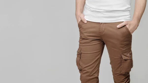 Gri arka planda elleri ceplerinde kahverengi kargo pantolonu giyen bir model, solda mesaj için boş bir yer. Model, şablon.