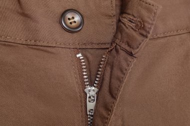 Kahverengi pantolonun kasıklarının fermuarını kapat. Giysi arka planı olarak dikişli kumaş, seçici odak.