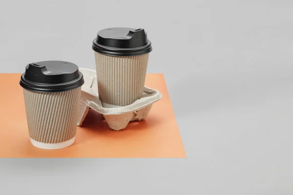 Paper cups of coffee on cardboard stand on orange and gray background, empty place for text. Takeaway coffee.