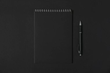 Boş siyah sayfaları olan boş bir defter ve koyu arkaplanlı bir kalem, kopyalama alanı, üst görünüm. İş veya eğitim kavramı.