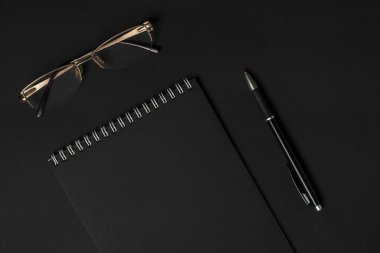 Siyah çarşaflı, beyaz sarmal ciltli siyah kalemli ve gözlüklü bir defter. İş veya eğitim asgari konsept.