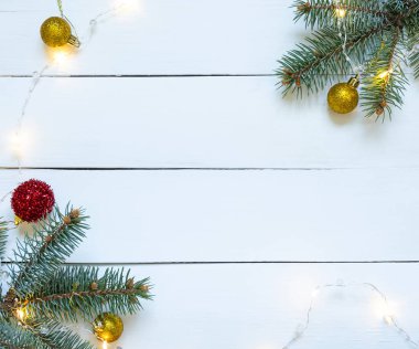 Beyaz ahşap arka planda, topları ve çelengi olan bir Noel ağacı dalı..