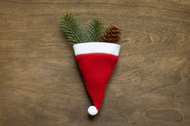 Noel ağacı dalları ve ahşap arka planda kırmızı Noel Baba şapkalı bir koni..