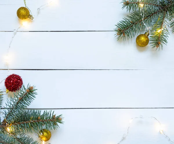 Beyaz ahşap arka planda, topları ve çelengi olan bir Noel ağacı dalı..
