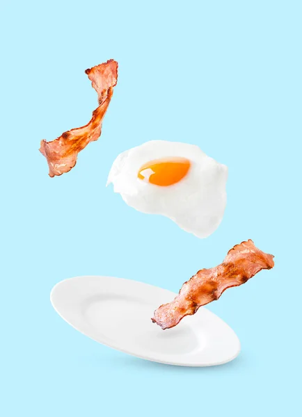 Бекон и яйцо, как английский завтрак левитат на тарелке на голубом фоне — стоковое фото