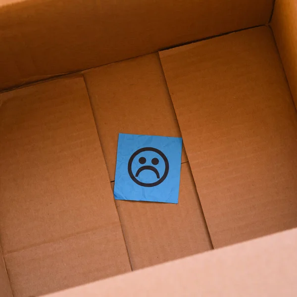 A blue paper note with a sad face on it in a cardboard box. Close up.