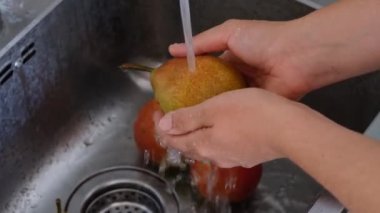Su kullanarak lavaboda armut yıkayan bir kadın. Kapat..