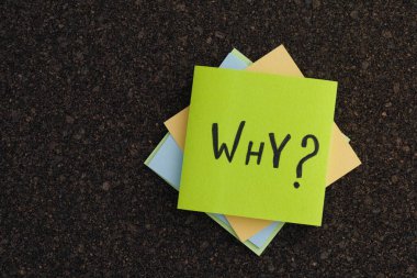 A stack of colorful sticky notes with the Why question on a cork board. Close up.