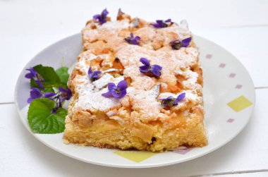 Kapalı menekşe çiçekleriyle süslenmiş bir tabak üzerinde bir parça kek.