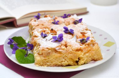 Elmalı turta üzerine pudra şekeri ve çiçek serpiştirilmiş.