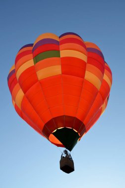 Mavi gökyüzünde renkli turuncu hava balonu havalanır.