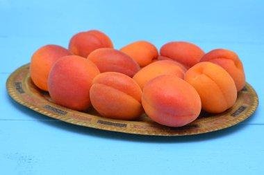 Mavi arka planda metal bir plaka üzerinde taze kayısılar.