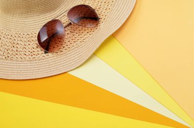 Parlak yaz arkaplanı, güneş gözlüğü ve sarı arka planda bir hasır şapka.