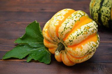 Koyu ahşap arka planda yapraklı, yenilebilir parlak bir balkabağı.