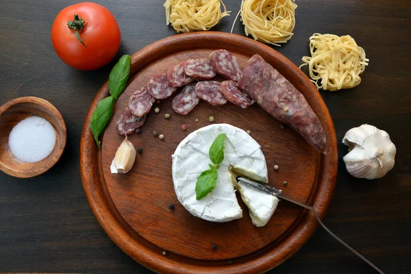 木製のテーブルの上にチーズとソーセージとイタリアのパスタ — ストック写真