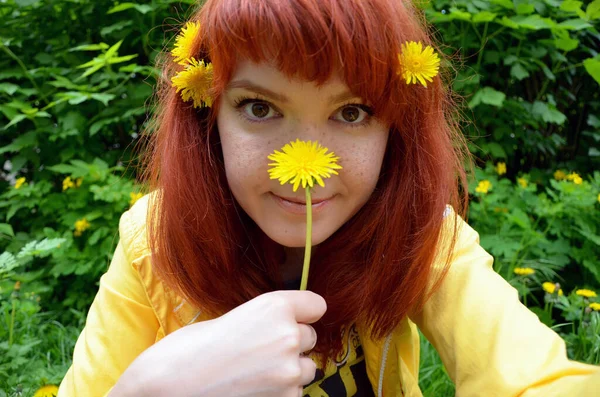 beautiful young redhead woman with yellow flowers in hair smiling at camera in park